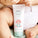 The image displays a tube of Tropic Little Emy Nappy Cream held by a baby, with their legs and diaper visible in the background. The packaging features a cute illustration of a pink bird, creating a playful and child-friendly design. The label highlights key ingredients such as tamanu oil, emu apple fruit extract, and zinc oxide, known for their soothing and protective properties. It is Certified Organic and Pediatrician Tested, emphasizing its safety and suitability for delicate baby skin.